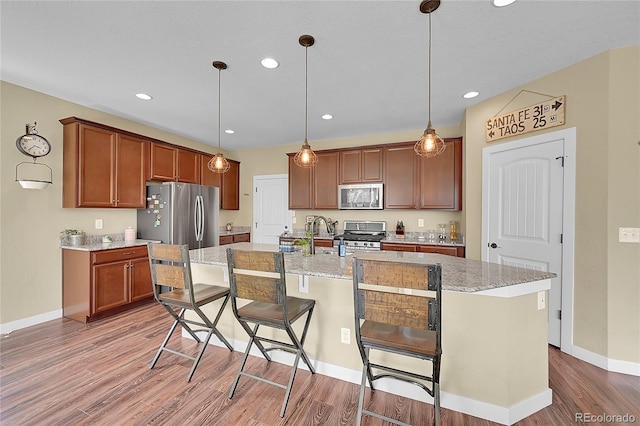 kitchen with a kitchen island with sink, a kitchen breakfast bar, light wood-style floors, appliances with stainless steel finishes, and hanging light fixtures