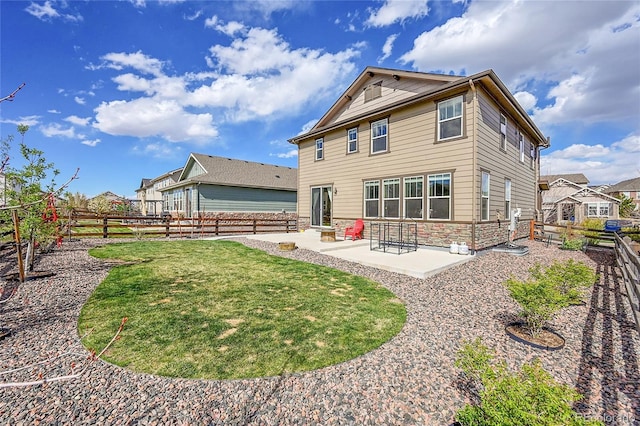 rear view of property with a lawn, stone siding, a patio area, and a fenced backyard