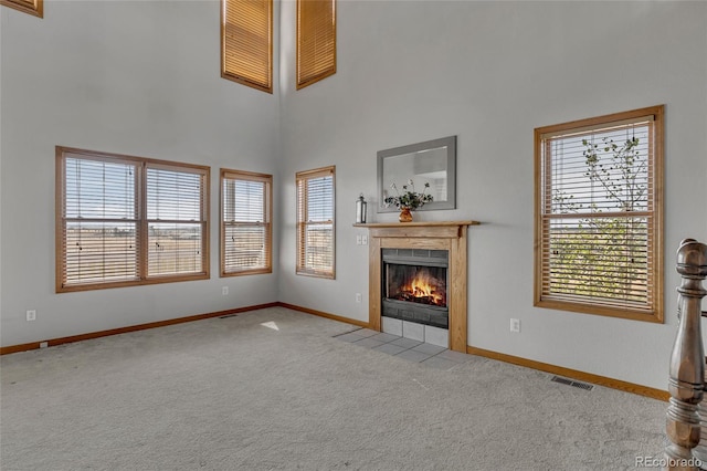 unfurnished living room with light carpet, a tiled fireplace, and a towering ceiling