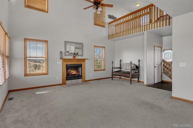 living room featuring carpet floors, a tiled fireplace, a high ceiling, and ceiling fan