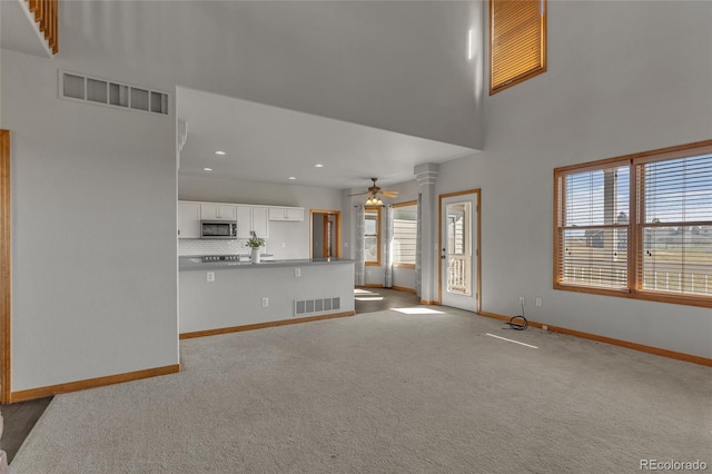 unfurnished living room with a towering ceiling, light carpet, decorative columns, and ceiling fan