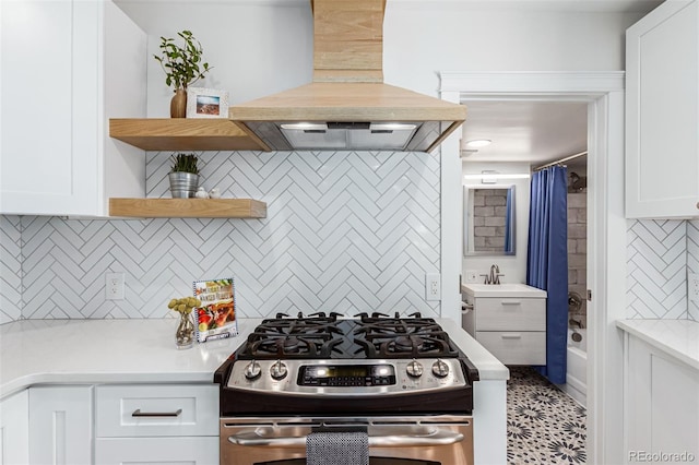 kitchen with tasteful backsplash, custom range hood, stainless steel gas range, white cabinets, and sink