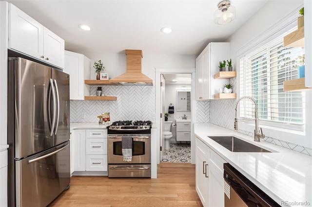 kitchen featuring appliances with stainless steel finishes, tasteful backsplash, custom range hood, white cabinetry, and sink