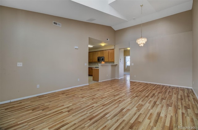 1343 Villa Grv, Monument, CO 80132 - unfurnished living room featuring light wood-type flooring, high vaulted ceiling, a chandelier, and baseboards