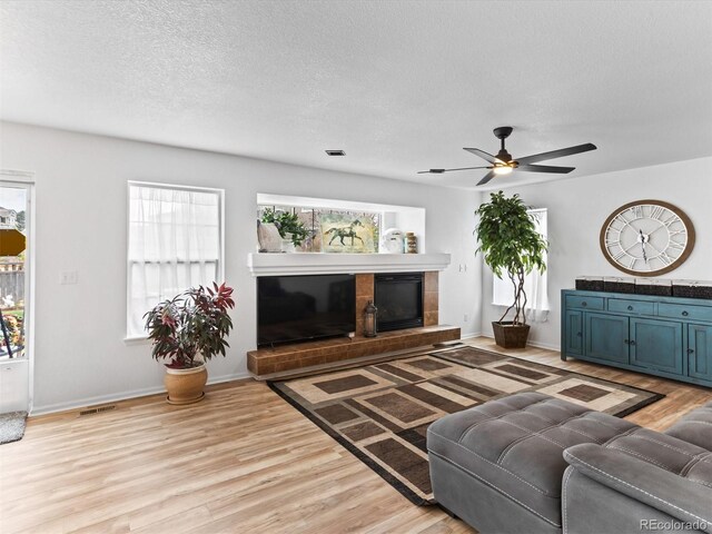 2468 Candleglow St, Castle Rock, CO 80109 - living room featuring a tiled fireplace, light wood-style floors, a ceiling fan, plenty of natural light, and a textured ceiling