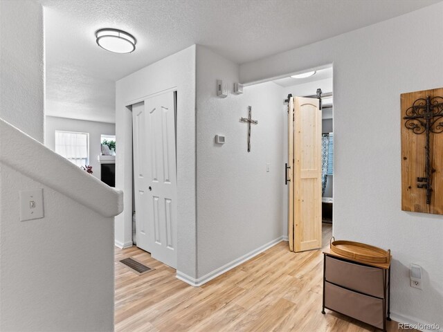 2468 Candleglow St, Castle Rock, CO 80109 - hall featuring light wood-style flooring, baseboards, a textured ceiling, and a barn door
