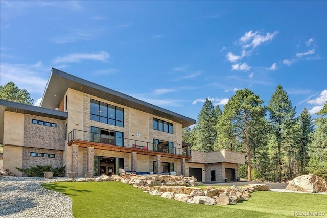 rear view of property featuring a garage, a yard, stone siding, and a balcony