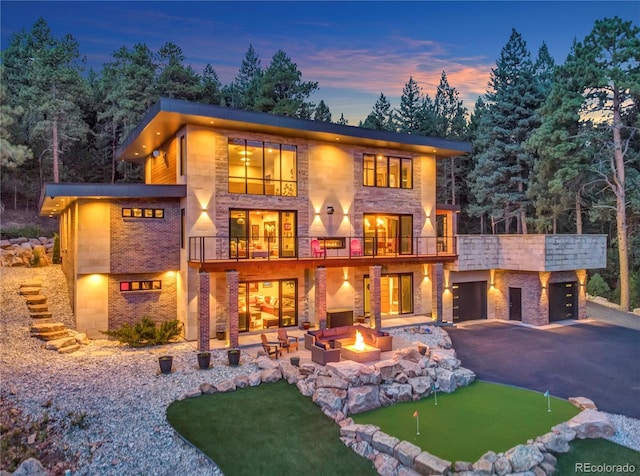 back of property at dusk featuring a patio, an outdoor fire pit, an attached garage, a balcony, and driveway