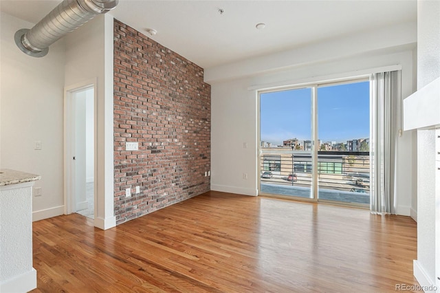 unfurnished living room featuring light wood-style floors, brick wall, a view of city, and baseboards