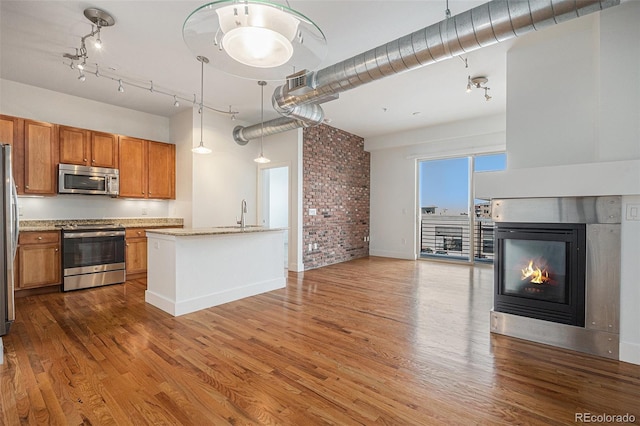 kitchen with brown cabinets, wood finished floors, appliances with stainless steel finishes, a glass covered fireplace, and light stone countertops