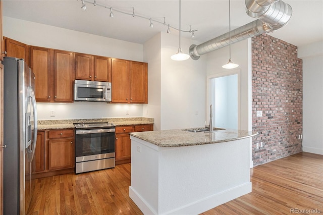 kitchen featuring light wood-type flooring, appliances with stainless steel finishes, brown cabinetry, and a sink