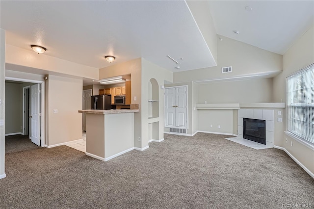 unfurnished living room with vaulted ceiling, light colored carpet, and a tile fireplace