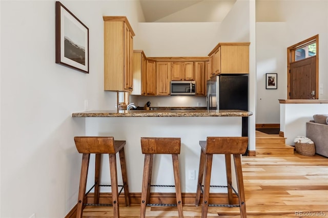 1152 Ski Hill Rd, Breckenridge, CO 80424 - kitchen featuring stainless steel microwave, a kitchen bar, a peninsula, light wood-style floors, and vaulted ceiling