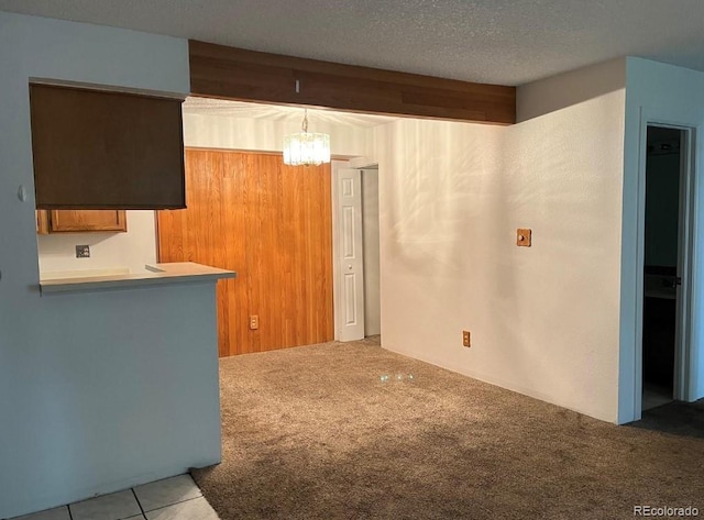 interior space featuring kitchen peninsula, decorative light fixtures, a notable chandelier, a textured ceiling, and light carpet