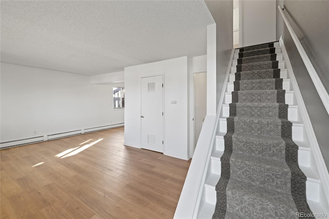 stairway featuring a textured ceiling, baseboard heating, and wood finished floors