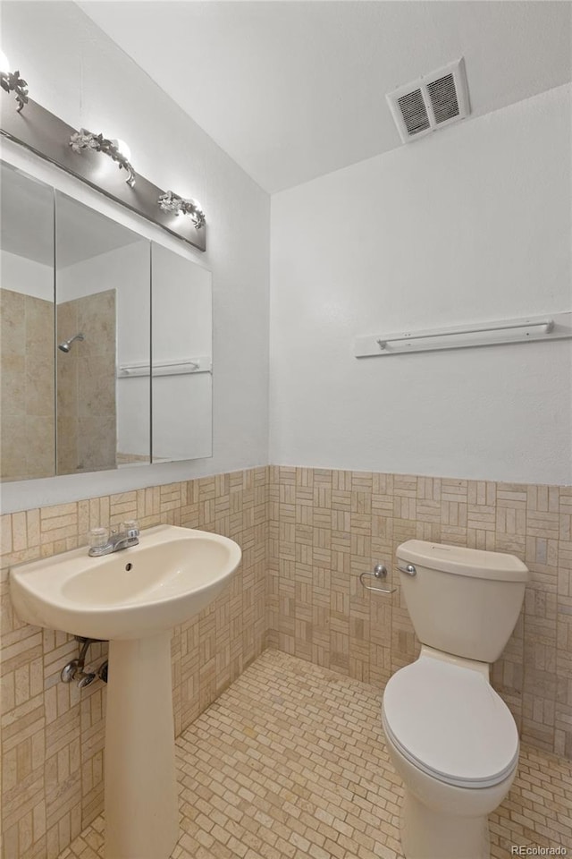 bathroom featuring visible vents, wainscoting, tile walls, toilet, and tile patterned floors