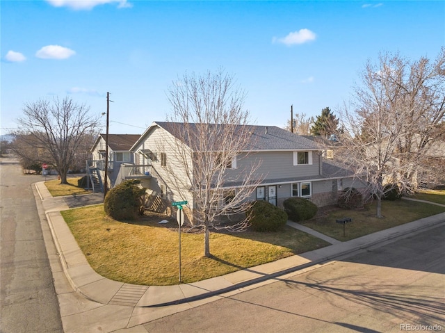 traditional home featuring stairway, concrete driveway, a front yard, and a shingled roof