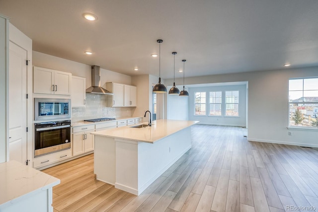 kitchen with a sink, decorative backsplash, appliances with stainless steel finishes, wall chimney range hood, and light wood-type flooring