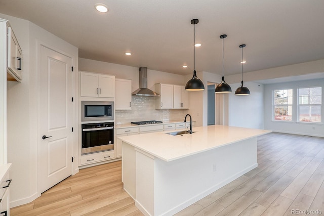 kitchen with gas cooktop, oven, built in microwave, wall chimney exhaust hood, and a sink