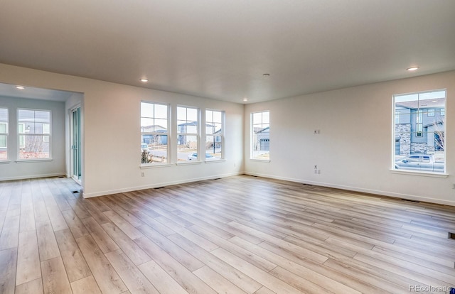 spare room with light wood finished floors, recessed lighting, a healthy amount of sunlight, and baseboards