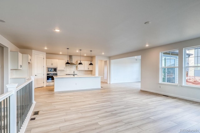 kitchen featuring built in microwave, open floor plan, light countertops, stainless steel oven, and wall chimney exhaust hood