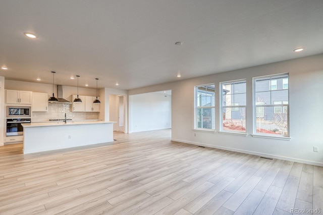 kitchen featuring oven, tasteful backsplash, open floor plan, wall chimney range hood, and built in microwave