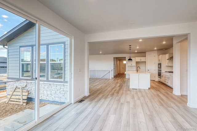 kitchen with a kitchen island with sink, light wood-type flooring, plenty of natural light, and white cabinets