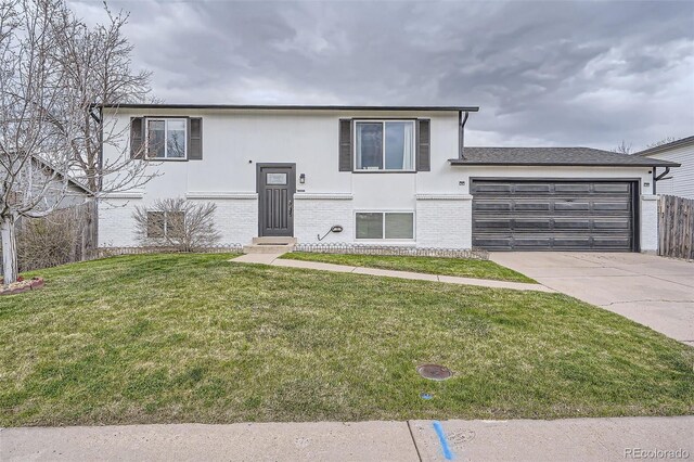 raised ranch featuring brick siding, a garage, stucco siding, a front yard, and driveway