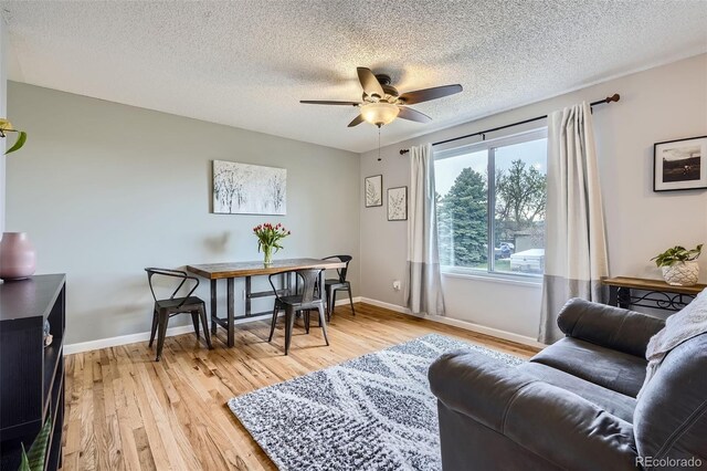 living area featuring baseboards, a textured ceiling, ceiling fan, and light wood-style flooring