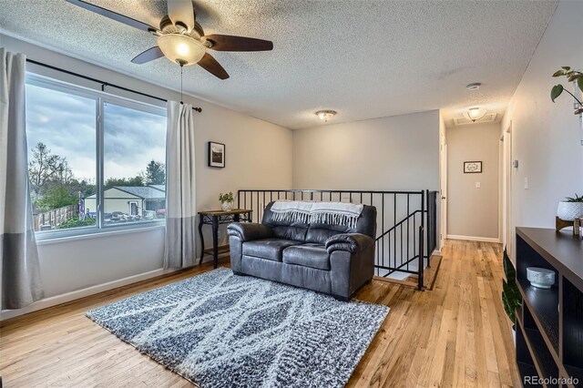 living room with baseboards, a textured ceiling, light wood finished floors, and ceiling fan
