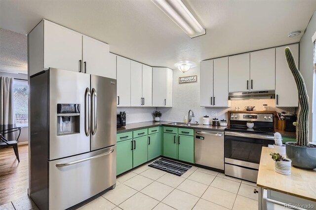 kitchen featuring appliances with stainless steel finishes, a sink, white cabinets, green cabinets, and under cabinet range hood