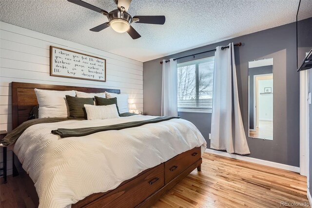 bedroom featuring wood walls, light wood-style flooring, a ceiling fan, and a textured ceiling