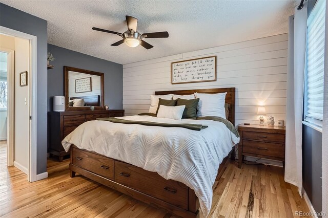 bedroom featuring wooden walls, ceiling fan, light wood-type flooring, and a textured ceiling