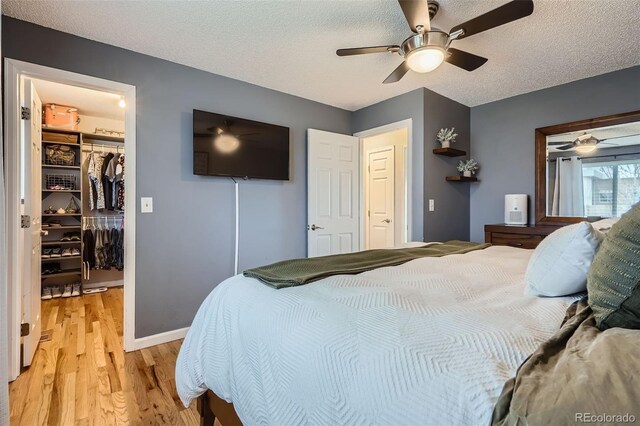bedroom featuring ceiling fan, a textured ceiling, a closet, a spacious closet, and light wood-style floors