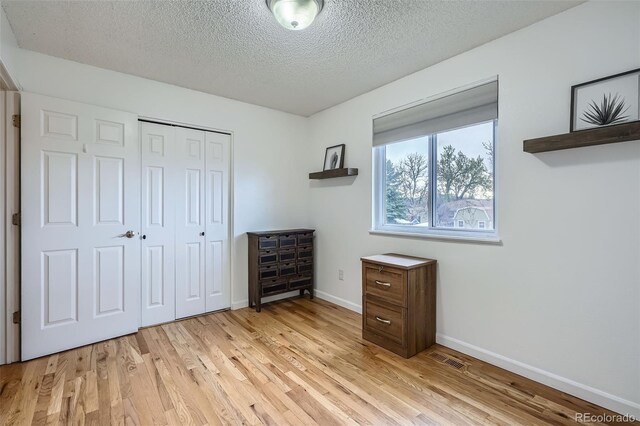 bedroom with light wood-style floors, a textured ceiling, baseboards, and visible vents