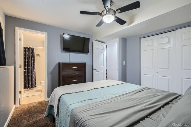 tiled bedroom with a closet, carpet flooring, a ceiling fan, and ensuite bath