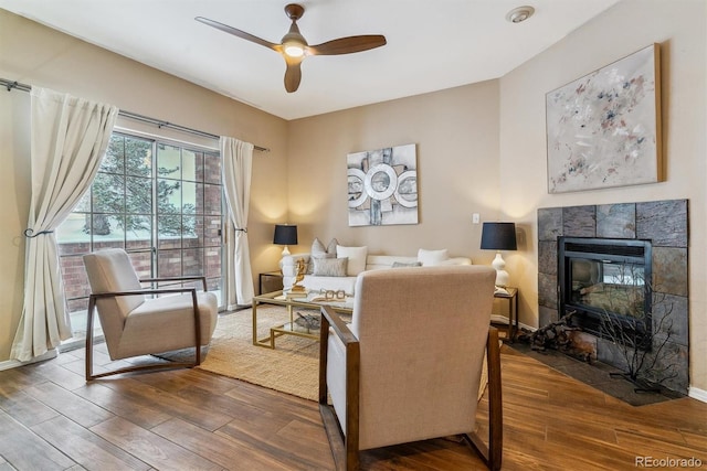 living room with ceiling fan, wood-type flooring, and a tile fireplace