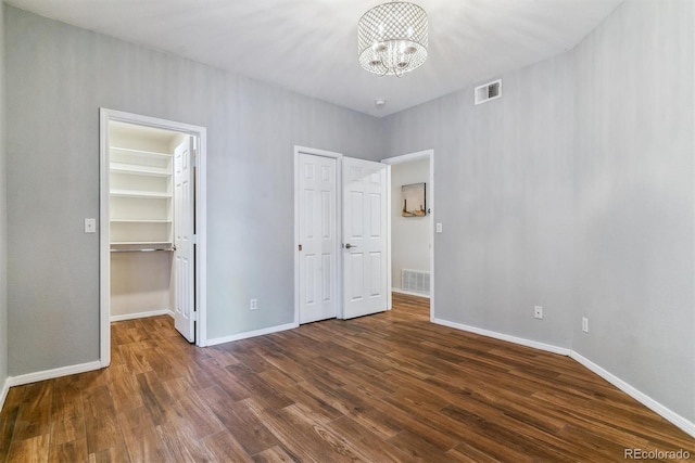 unfurnished bedroom with a spacious closet, dark hardwood / wood-style flooring, a closet, and a notable chandelier