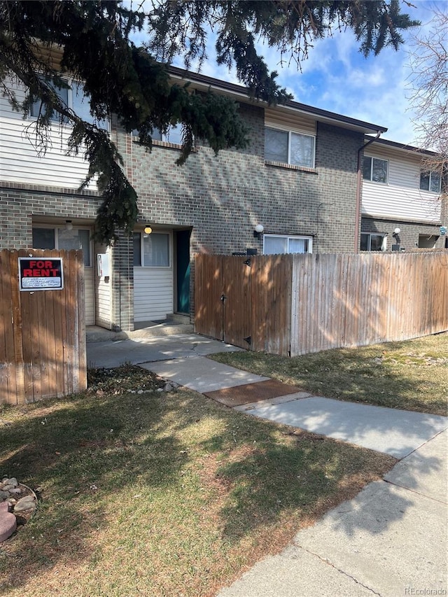 exterior space featuring brick siding, a front lawn, and fence