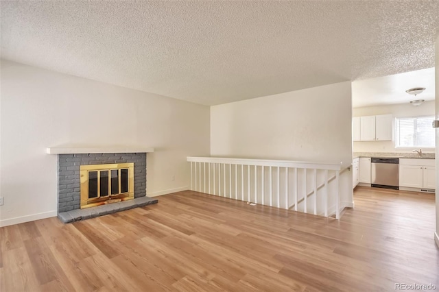 4182 S Joplin St, Aurora, CO 80013 - unfurnished living room with light wood-style flooring, a textured ceiling, baseboards, a brick fireplace, and a sink