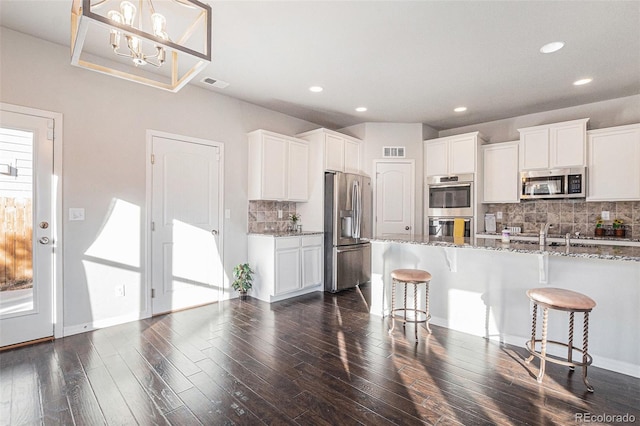 kitchen with a breakfast bar, decorative backsplash, light stone countertops, white cabinetry, and stainless steel appliances