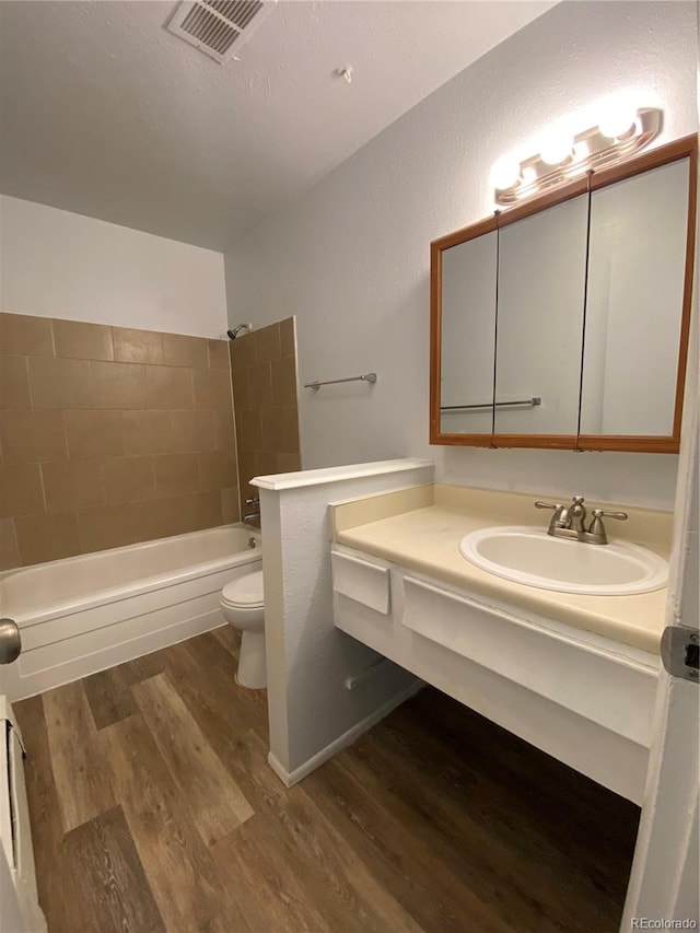 full bathroom with hardwood / wood-style flooring, toilet, tiled shower / bath combo, vanity, and a textured ceiling