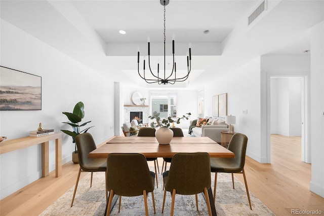 3301 Arapahoe Ave Unit 411, Boulder, CO 80303 - dining room featuring a chandelier, a warm lit fireplace, light wood-style floors, and a raised ceiling