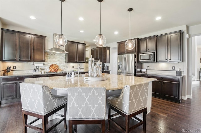 25548 E Fair Dr, Aurora, CO 80016 - kitchen featuring appliances with stainless steel finishes, wall chimney exhaust hood, dark brown cabinetry, a large island with sink, and a kitchen bar