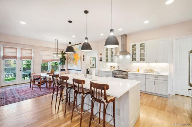 1455 Flowers Ct, Erie, CO 80516 - kitchen featuring stainless steel stove, a center island with sink, wall chimney range hood, and light wood-type flooring