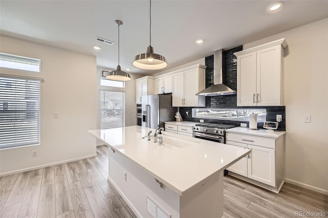 kitchen featuring a sink, high quality appliances, hanging light fixtures, light countertops, and wall chimney exhaust hood