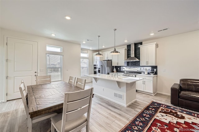 kitchen featuring pendant lighting, a center island with sink, wall chimney exhaust hood, light countertops, and high end refrigerator