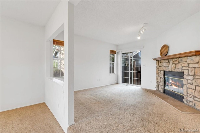 unfurnished living room featuring a textured ceiling, a stone fireplace, carpet floors, and track lighting