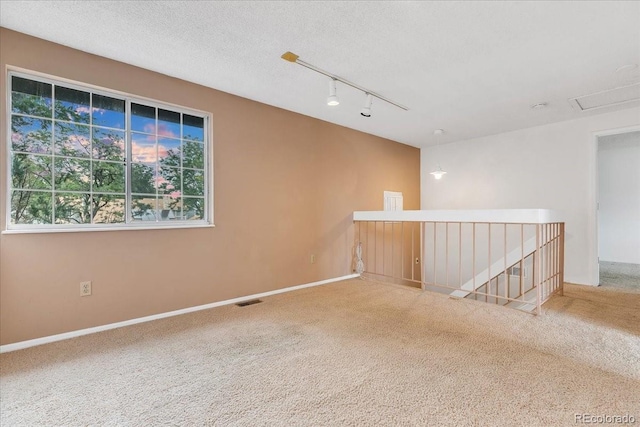 carpeted spare room with a textured ceiling and rail lighting