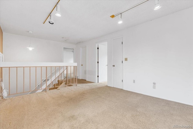 spare room featuring a textured ceiling, rail lighting, and light carpet